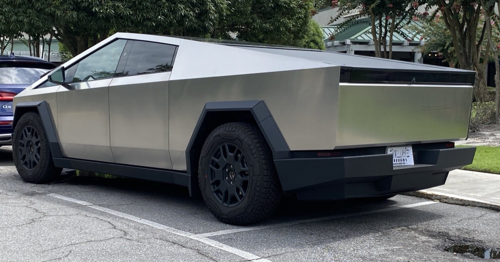 Rear three-quarter view of a stainless Tesla Cybertruck parked in a lot with its tailgate closed